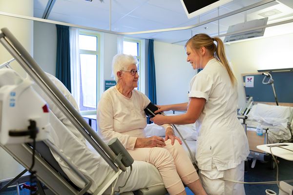 Verpleegkundige helpt patiënt aan bed